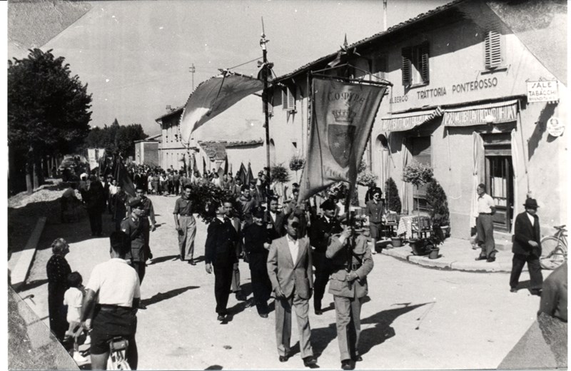 Un corteo (1954) torna in paese doppo essere stato alla Cappella dei partigiani al cimitero della Misericordia. Transita  davanti all’Albergo Ponterosso dove dieci anni prima lavorava Domenico Trifirò
