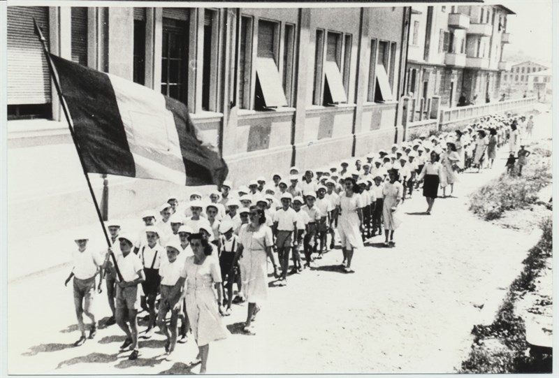 Fine anni ’40 del ‘900. Gli alunni tornano in classe dopo una gita per la campagna. In  testa, immancabile, il tricolore.